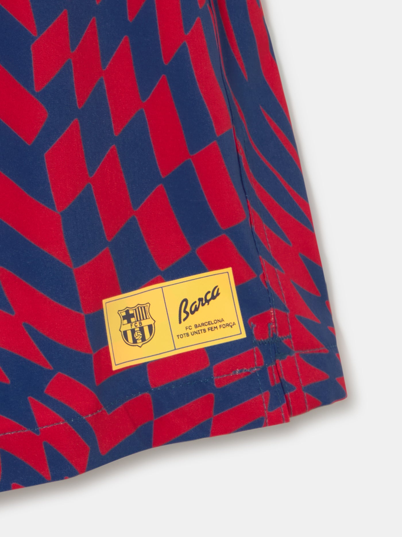 FC Barcelona swim shorts with a bold red and blue optical illusion checkerboard pattern, featuring an elastic waistband with drawstring and a yellow patch logo near the hem.