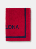 Red FC Barcelona towel featuring the word "Barça" in large navy script, with "TOTS UNITS FEM FORÇA" vertically on the left and "FC BARCELONA" with club crest on the right side