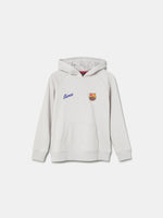 White FC Barcelona hoodie featuring a unique back design with a four-petal flower made of circular emblems: the St. George cross, Catalan flag, blaugrana stripes, and a central golden football. Below the graphic, the text reads “Futbol Club Barcelona” and “Més que un club” along with minimalist logos.