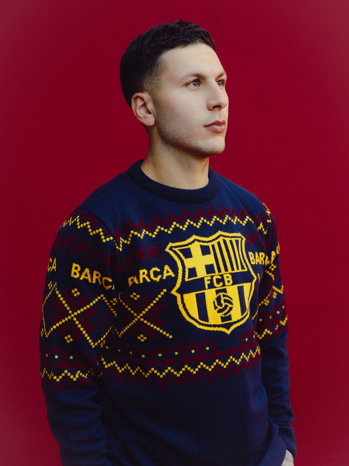 Homme portant un pull marine FC Barcelona avec motifs géométriques jaunes et grenat et un grand écusson Barça sur la poitrine.
