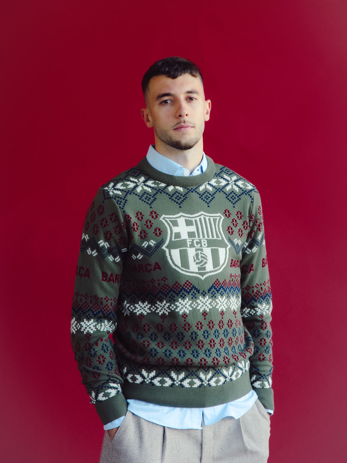 Vue de face d’un modèle portant un pull gris FC Barcelona avec un grand écusson du club et une maille à motif sur fond rouge.