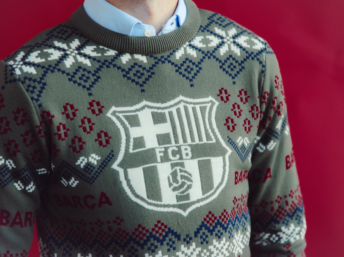 Vue de face d’un pull en maille gris du FC Barcelona avec des motifs géométriques bleus, blancs et rouges et un grand blason du Barça sur la poitrine