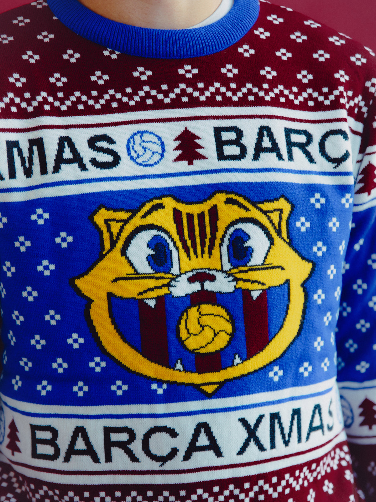 Primer plano de un jersey navideño de FC Barcelona con estampado azul y granate, texto Barça XMAS y un gran gráfico de cara de gato en la parte delantera.