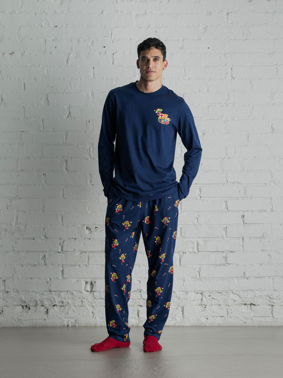 Vue de face d’un modèle portant un haut à manches longues bleu marine de FC Barcelona et un pantalon de détente imprimé assorti avec des chaussettes rouges.