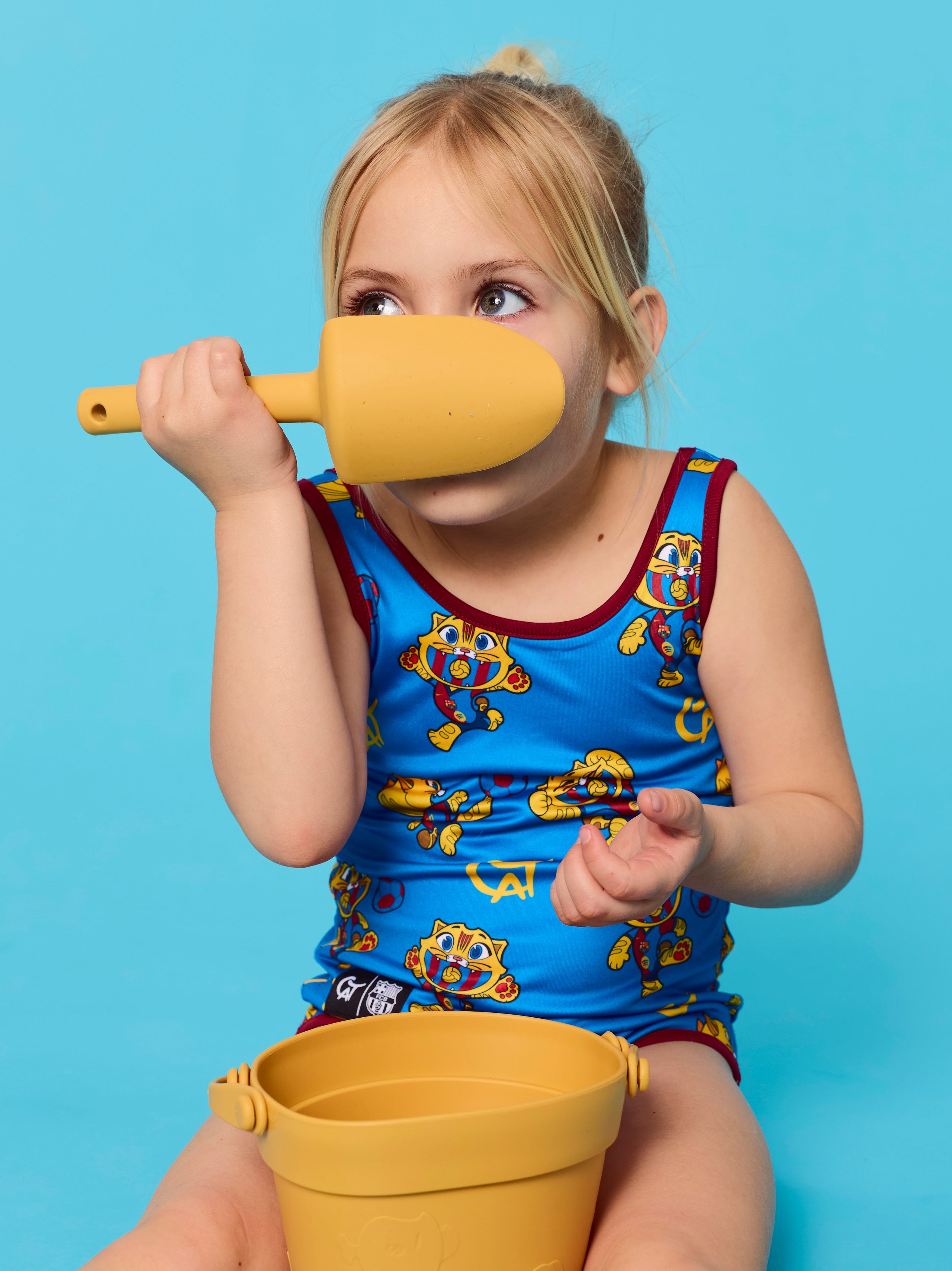 Child playing with a yellow shovel and bucket against a blue background