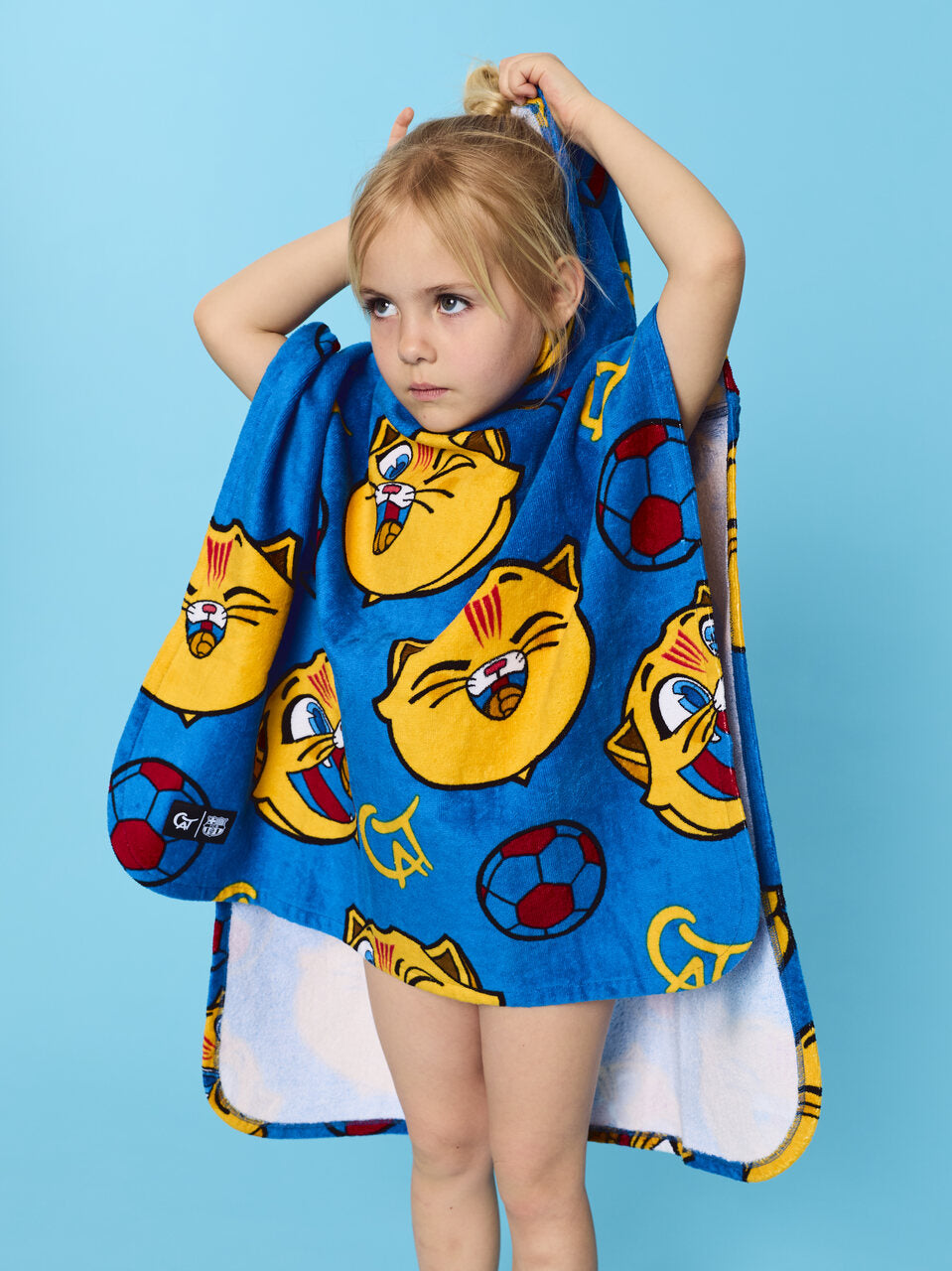 Child wearing a blue towel with cartoon cat faces on a blue background