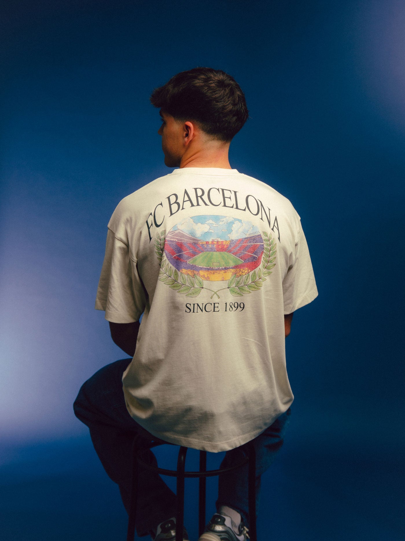 Cream T-shirt with large FC Barcelona stadium graphic, laurel wreath design, and 'FC Barcelona Since 1899' text on the back