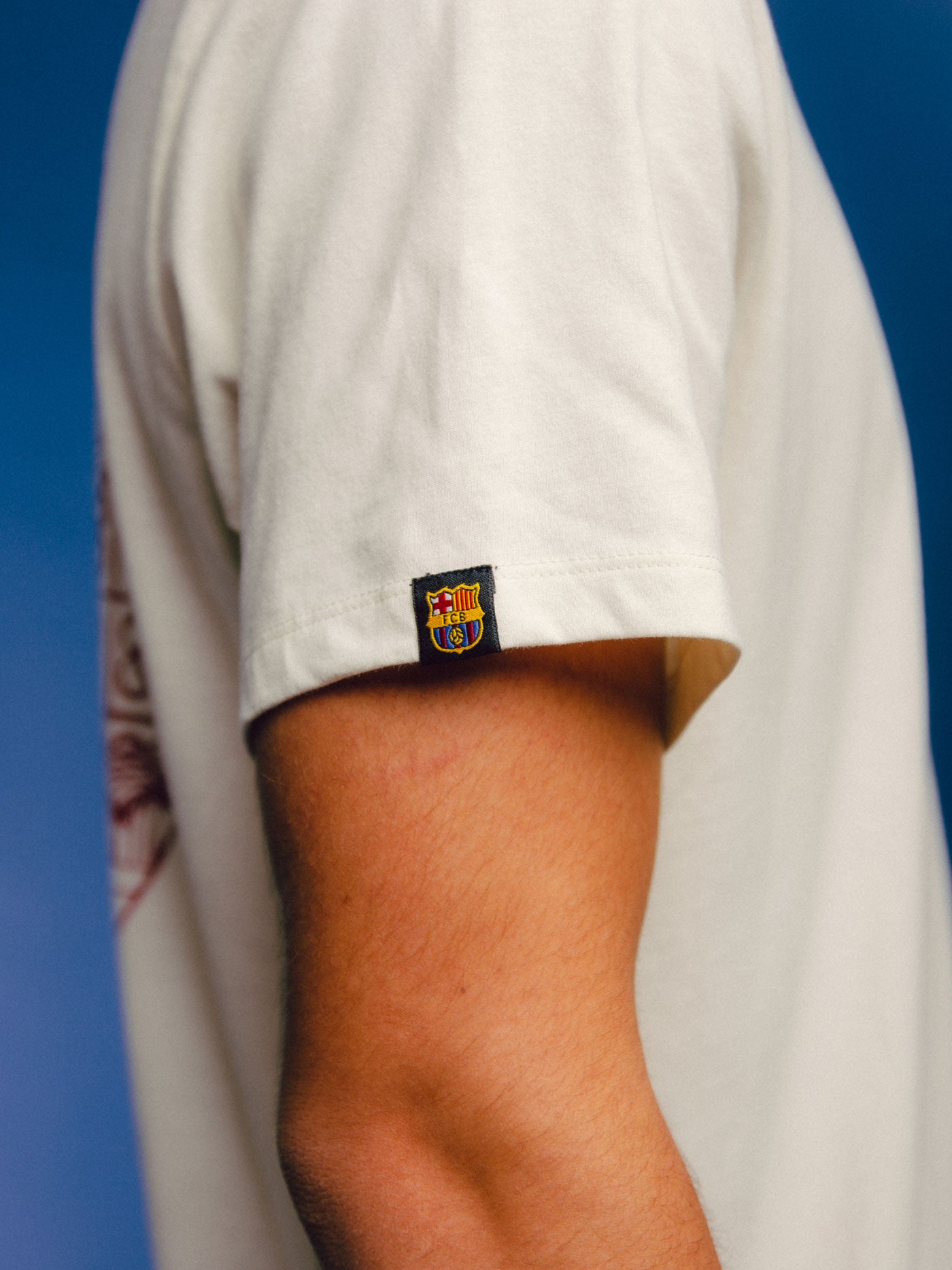  off-white FC Barcelona t-shirt with a red artistic illustration on the back, featuring iconic landmarks of Barcelona and the Camp Nou stadium inside a stylized club crest.
