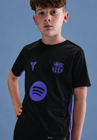 Child wearing a black t-shirt with purple logos against a blue background