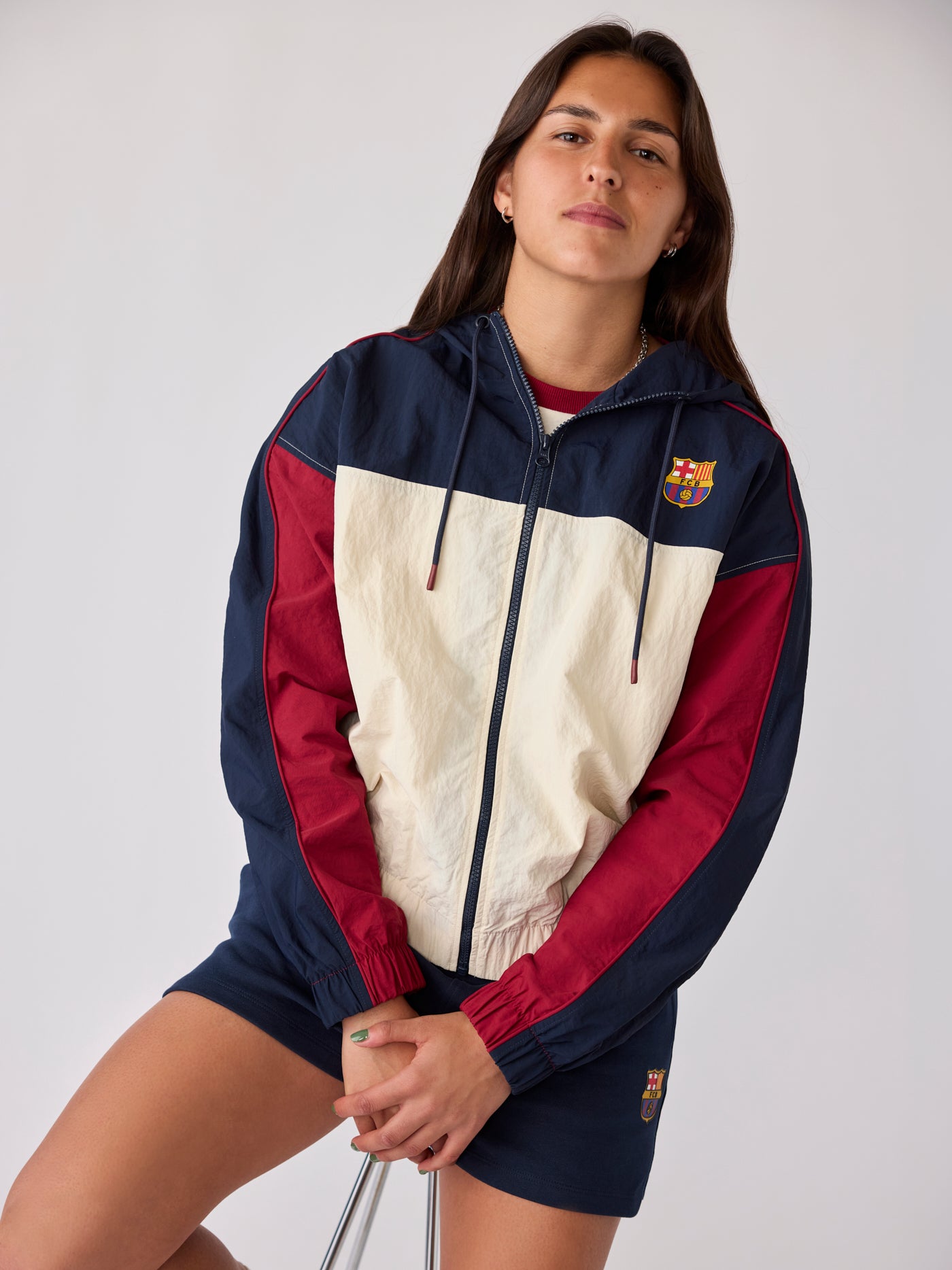 Model wearing a Barça colour-block windbreaker jacket and navy shorts with crest details.