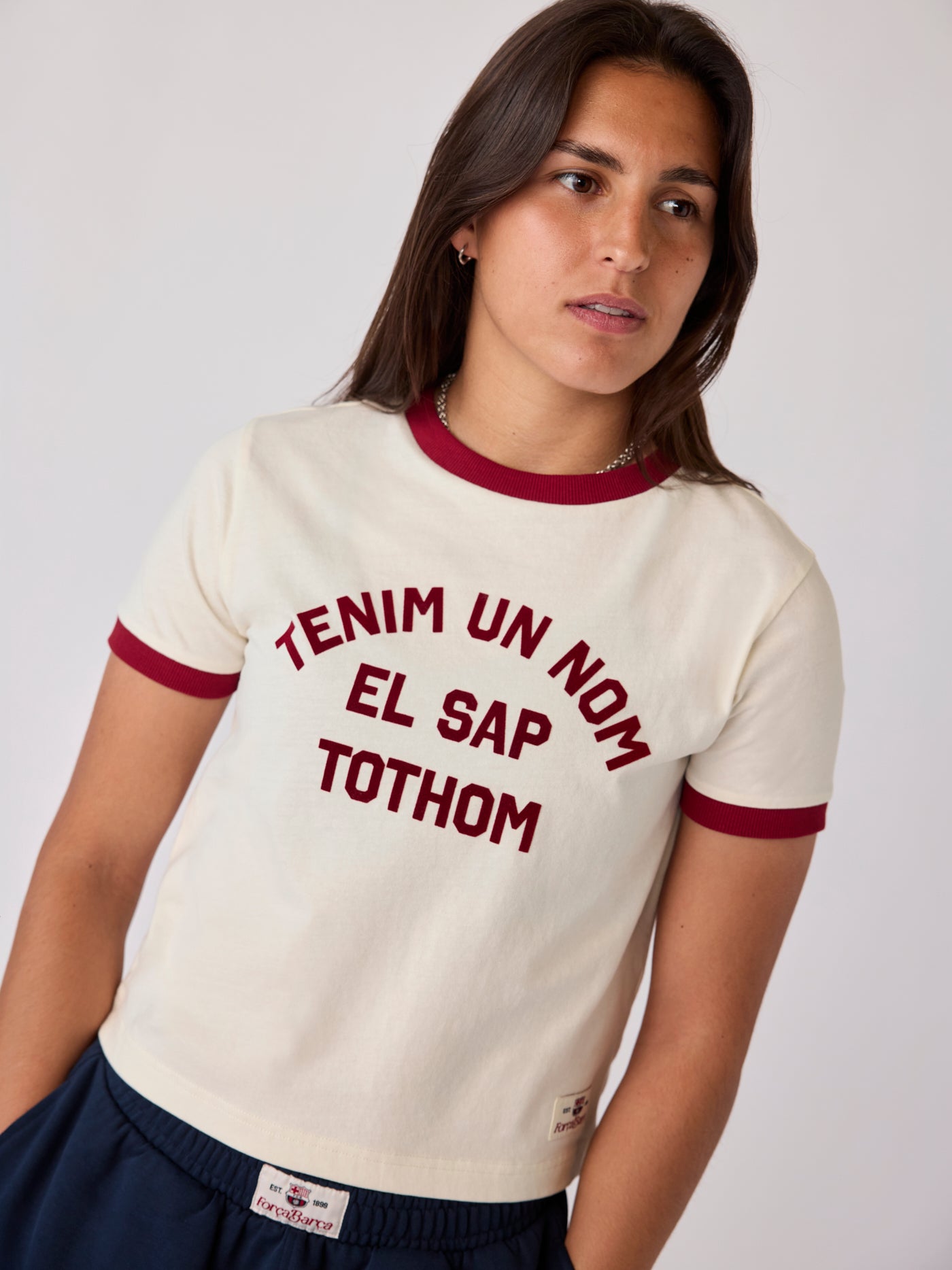 Model wearing a cream Barça T-shirt with burgundy trim and Catalan text graphic.