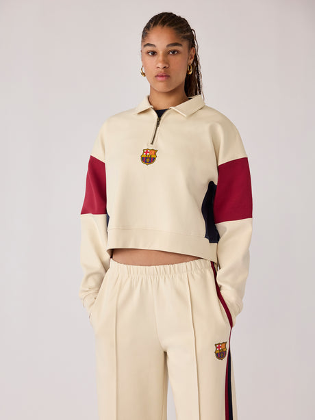 Model wearing a cream Barça cropped half-zip sweatshirt and matching trousers with crest details.