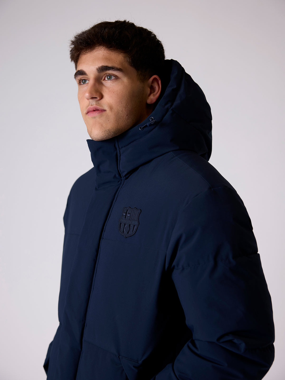 Model wearing a navy FC Barcelona hooded jacket with a high collar and the club crest on the chest.
