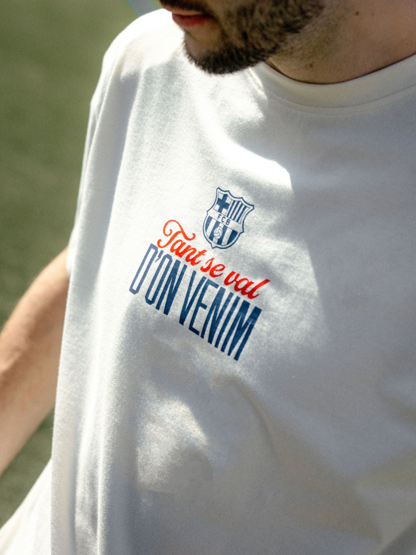 White t-shirt with blue and red text and logo on a blurred natural background