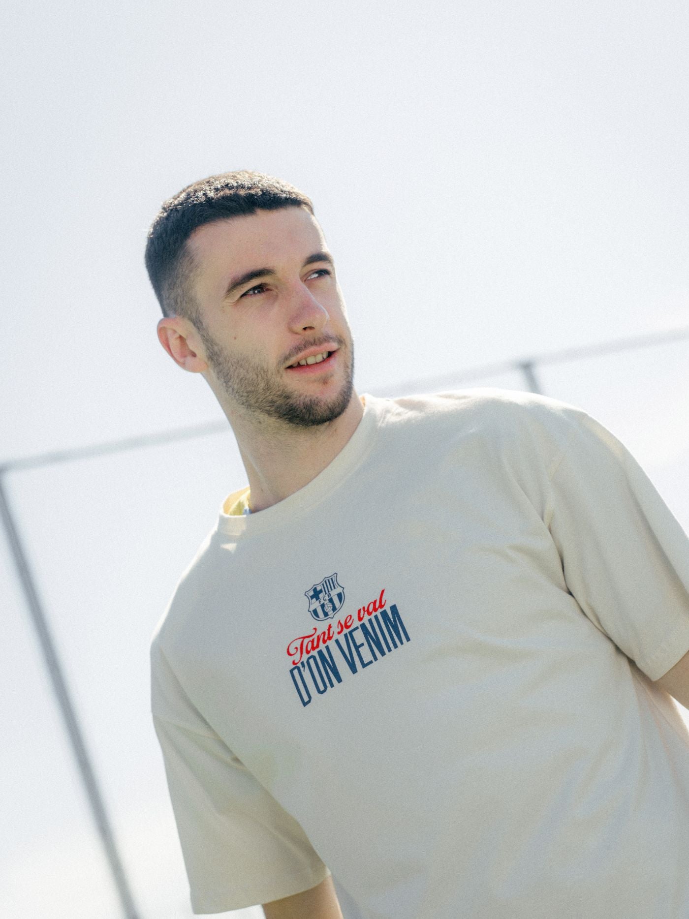Man wearing a beige t-shirt with text, standing outdoors against a light background