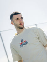 Man wearing a beige t-shirt with text, standing outdoors against a light background