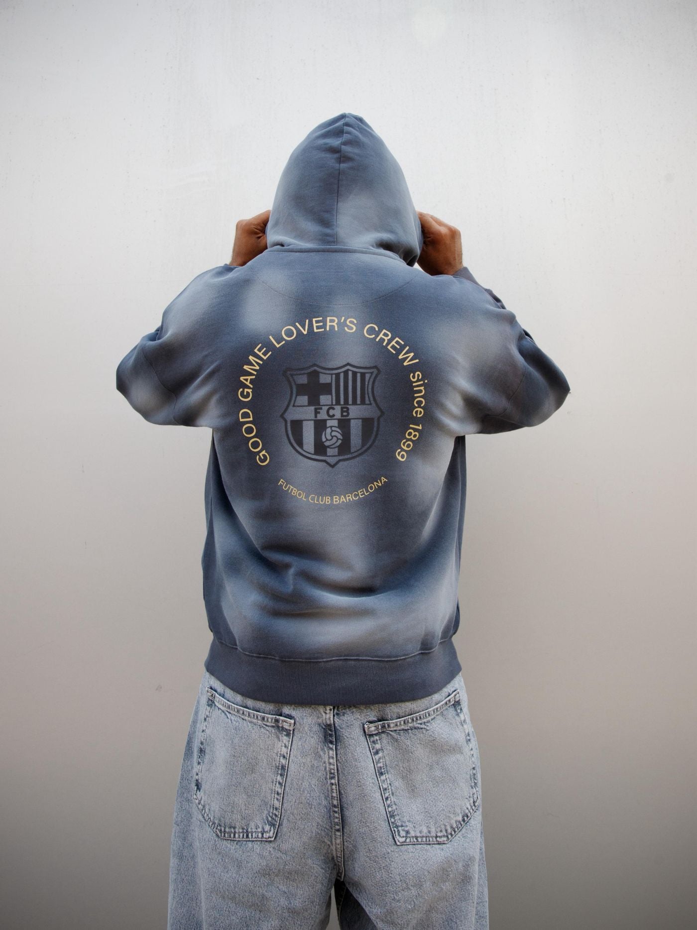Man wearing a dark blue FC Barcelona hoodie with golden minimalist 'Barça' symbols printed on the chest