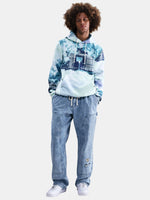 Person wearing a tie-dye hoodie and blue jeans on a white background