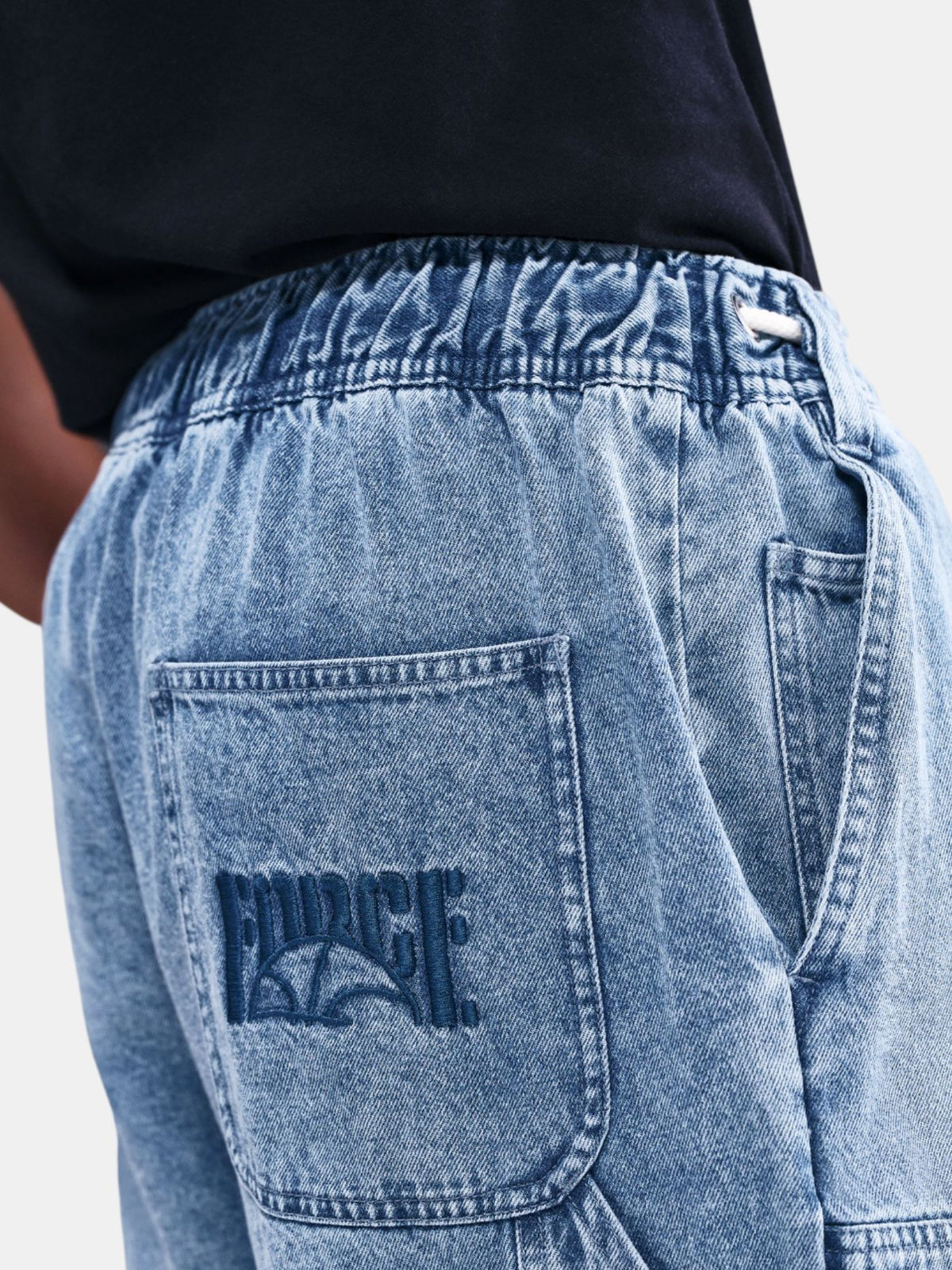 Close-up of blue jeans with a brand logo on the pocket against a neutral background