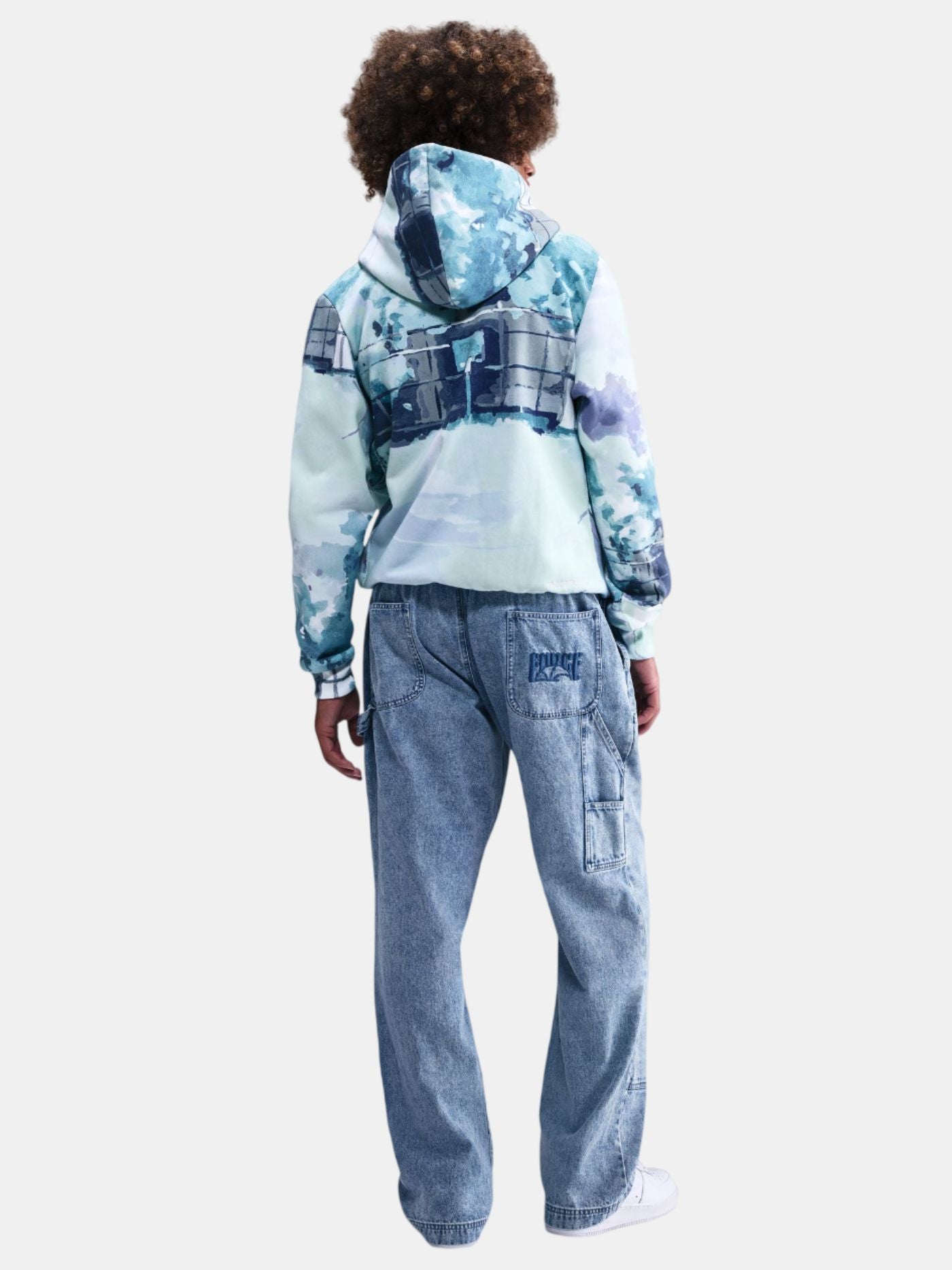 Person wearing a blue tie-dye hoodie and jeans on a white background