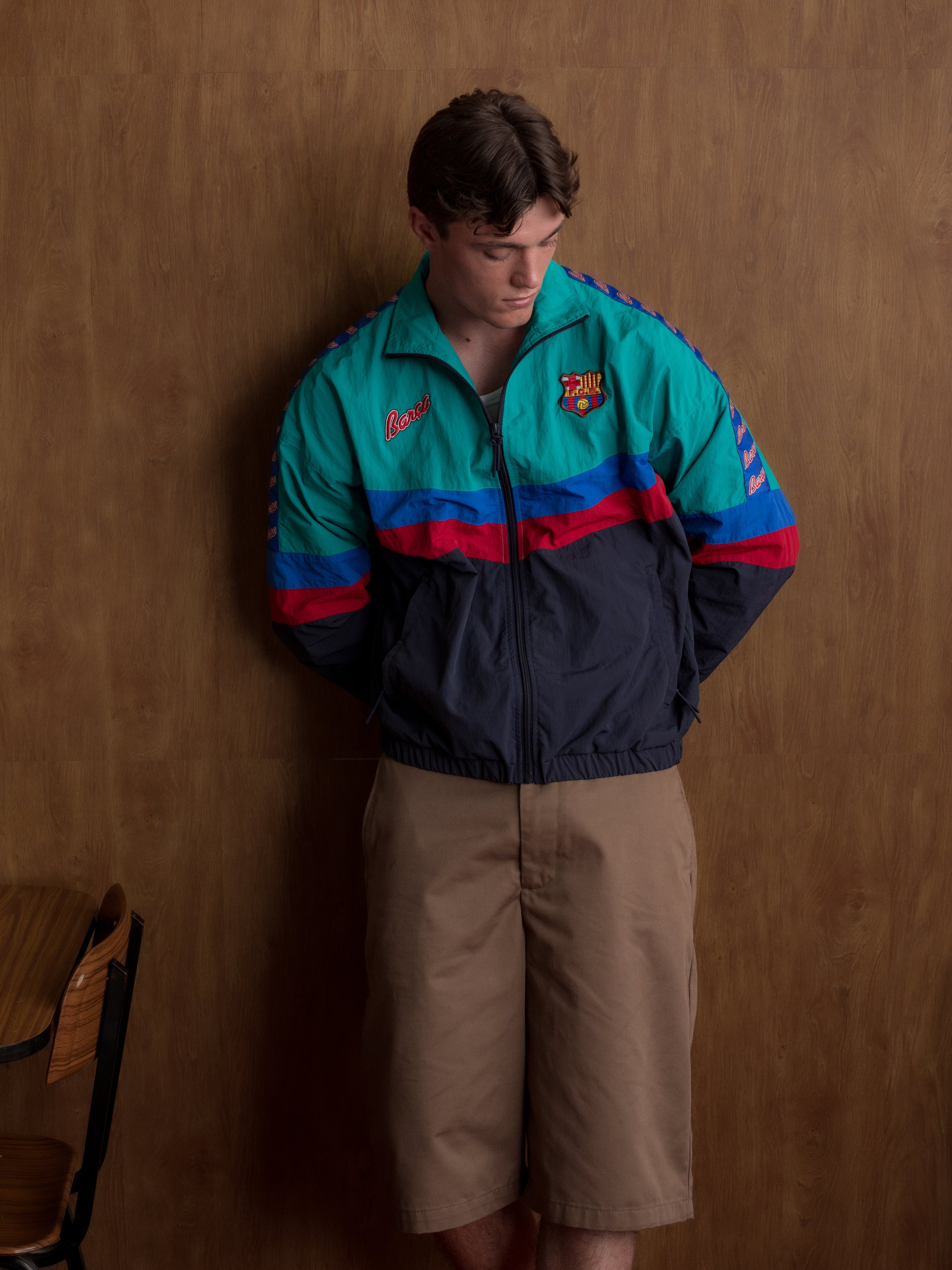 Retro-style windbreaker in teal, red, blue, and navy with FC Barcelona crest and embroidered 'Barça' text on the chest.