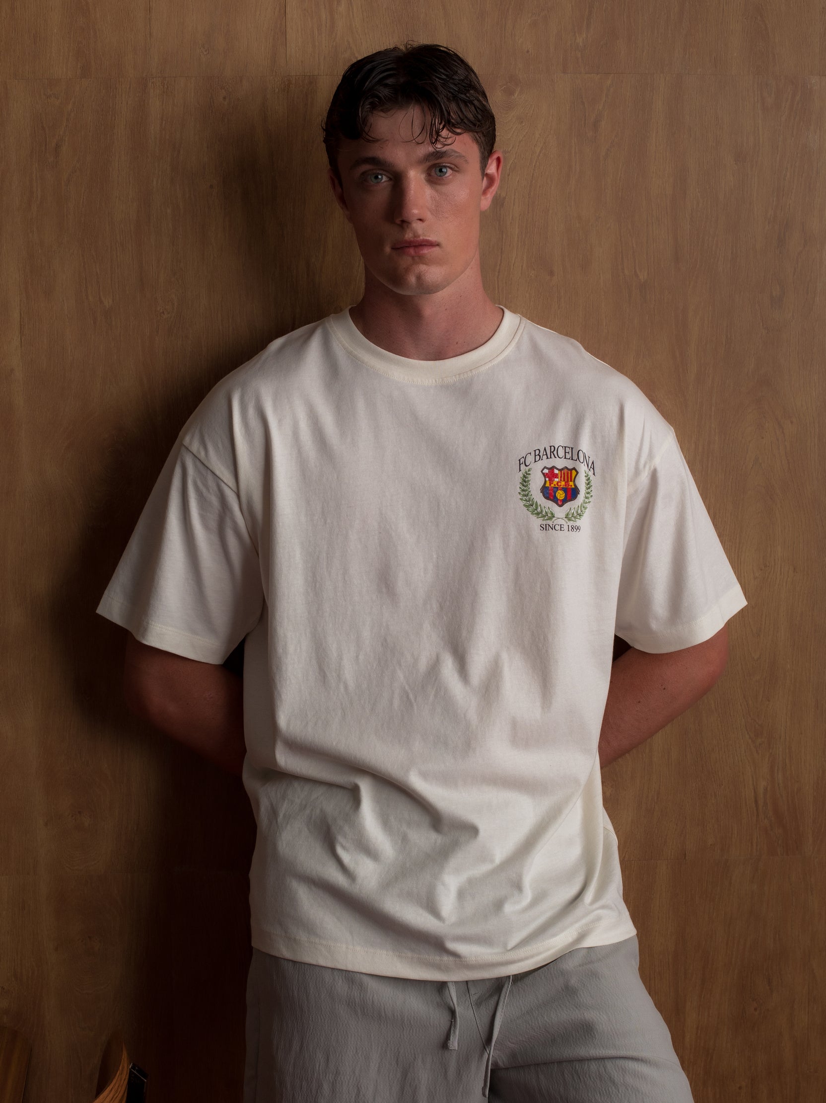 Cream T-shirt with large FC Barcelona stadium graphic, laurel wreath design, and 'FC Barcelona Since 1899' text on the back