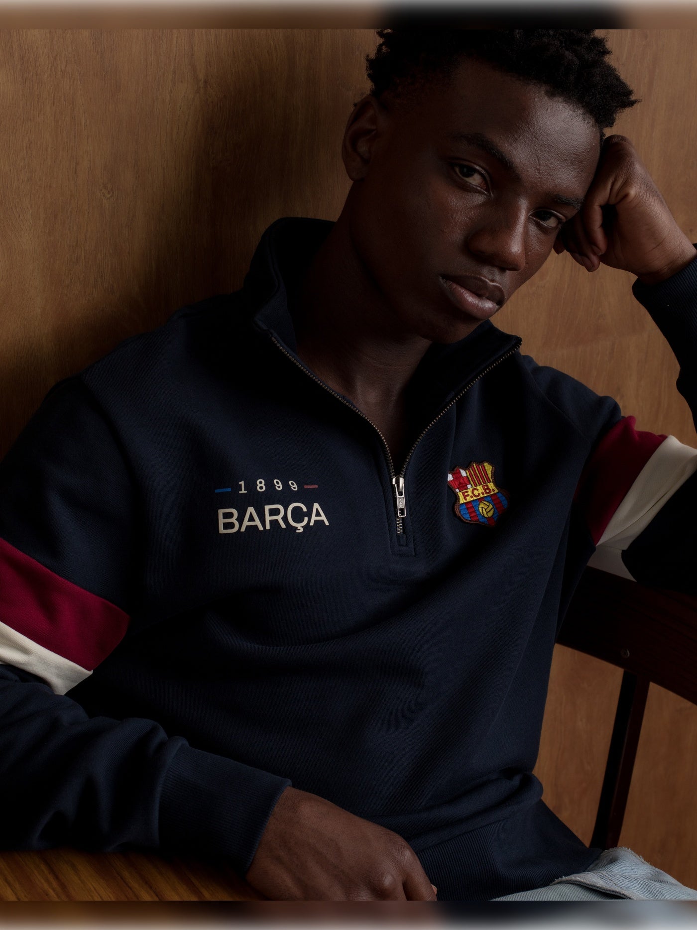 Man wearing a navy half-zip pullover with the FC Barcelona crest and '1899 Barça' text on the chest, featuring red and white stripes on the sleeves