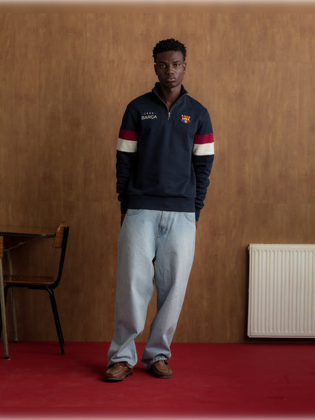 Man wearing a navy half-zip pullover with the FC Barcelona crest and '1899 Barça' text on the chest, featuring red and white stripes on the sleeves