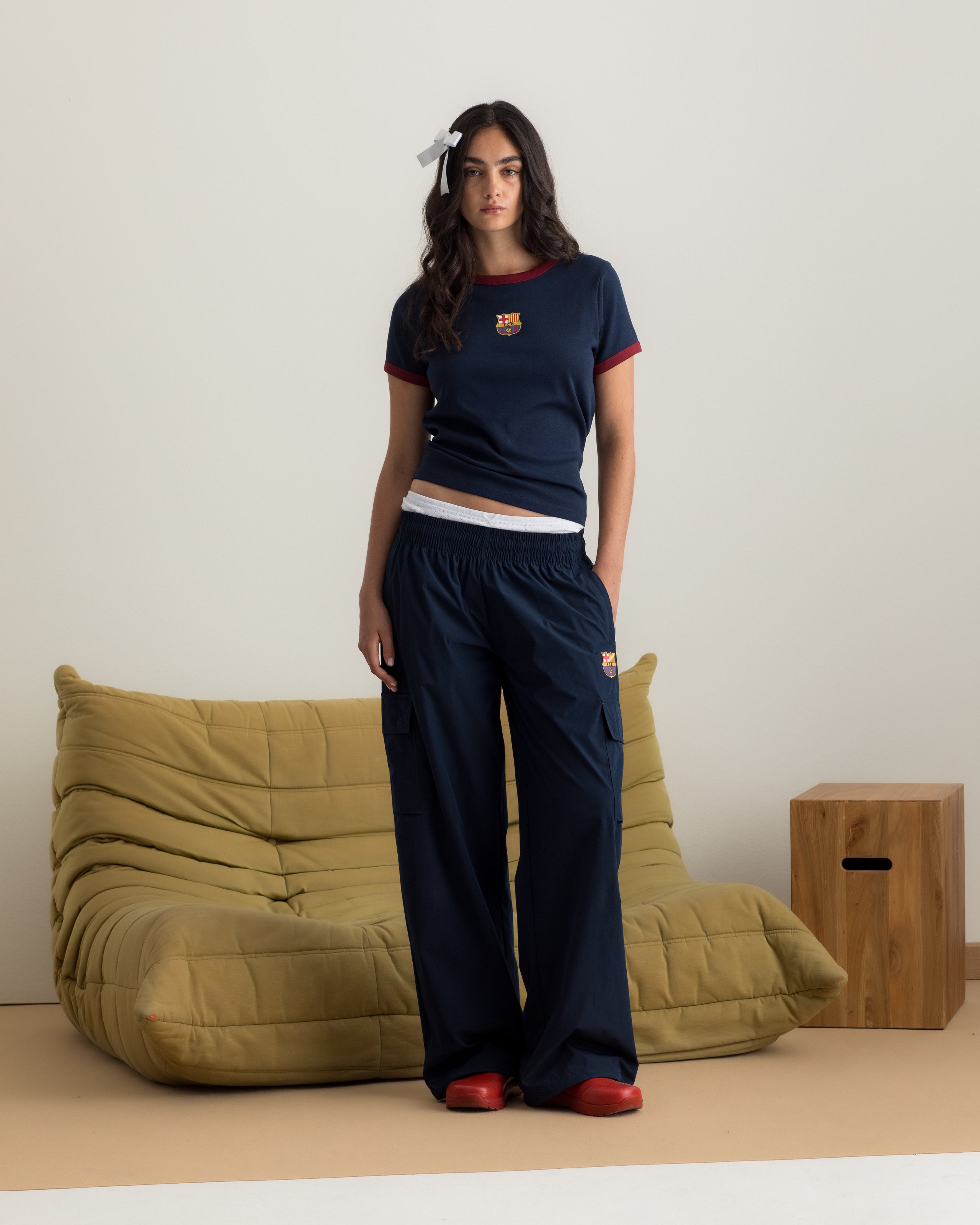 Model wearing a navy blue FC Barcelona T-shirt with red trim and club crest, paired with matching navy cargo pants featuring embroidered crest