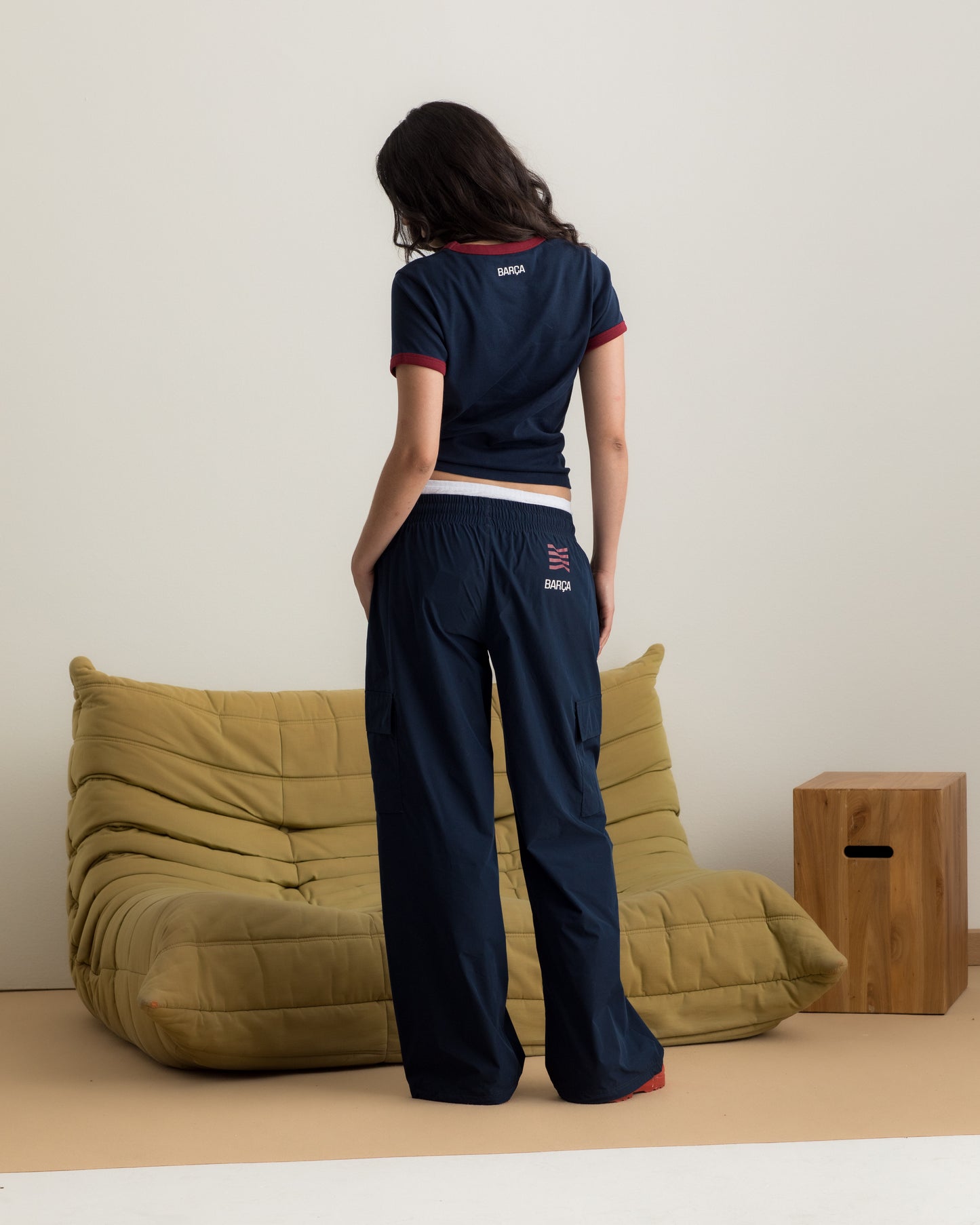 Model wearing a navy blue FC Barcelona T-shirt with red trim and club crest, paired with matching navy cargo pants featuring embroidered crest
