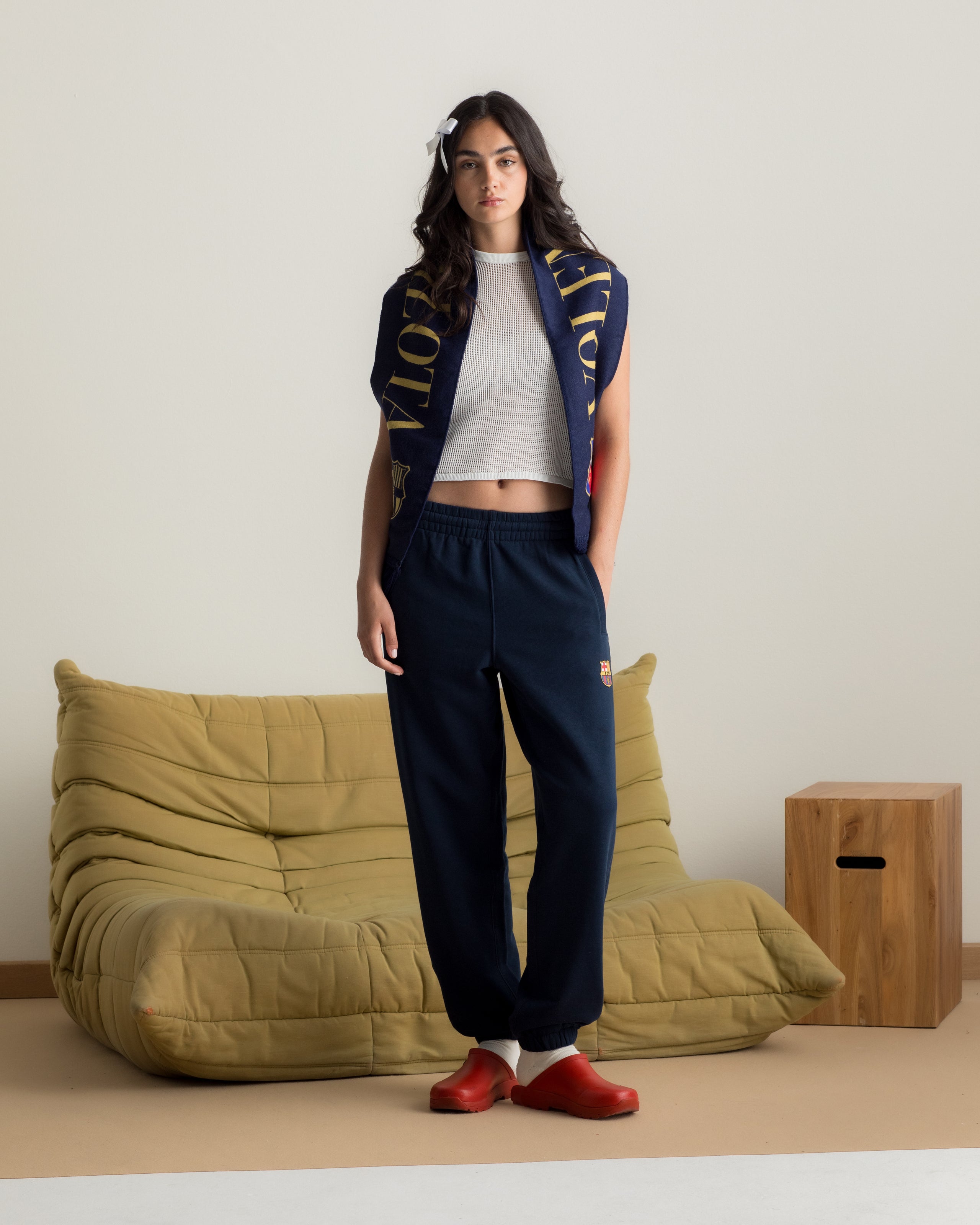 Model wearing navy blue FC Barcelona sweatpants with embroidered crest, paired with a white crop top and a navy scarf with gold lettering