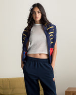 Model wearing navy blue FC Barcelona sweatpants with embroidered crest, paired with a white crop top and a navy scarf with gold lettering