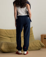 Model wearing navy blue FC Barcelona sweatpants with embroidered crest, paired with a white crop top and a navy scarf with gold lettering