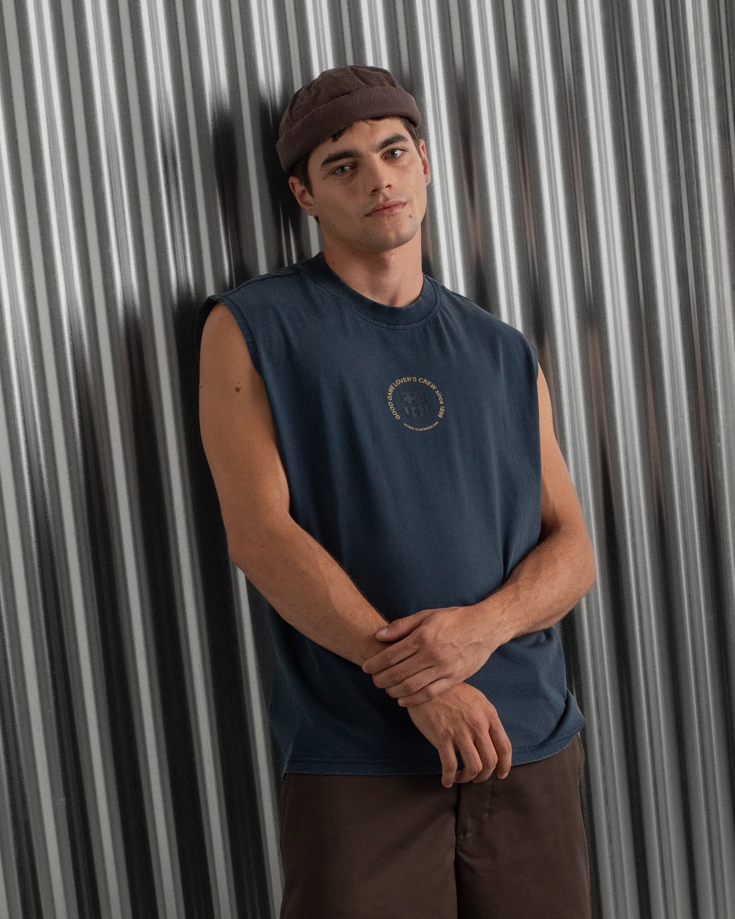 sleeveless navy blue FC Barcelona t-shirt with a small circular crest and text detail on the chest, paired with dark pants.