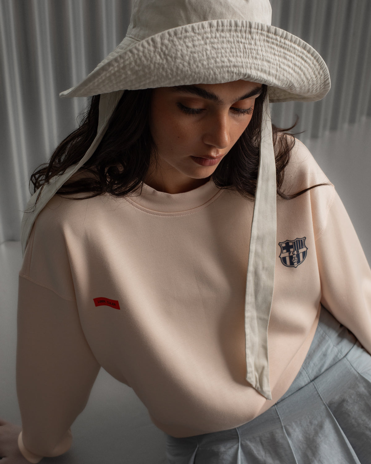 Light pink FC Barcelona sweatshirt with navy club crest on the chest and a small red rectangular detail on the left side.