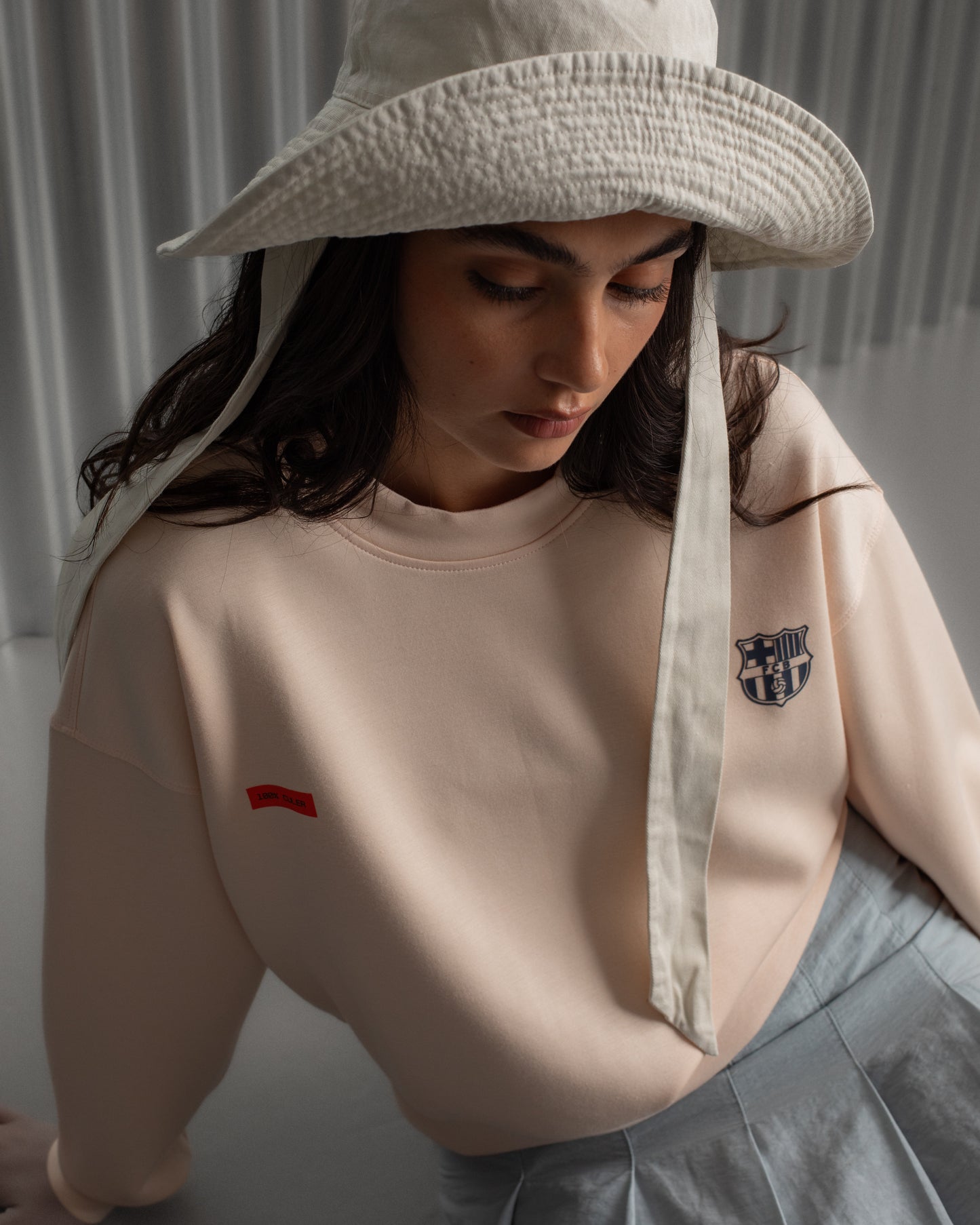 Light pink FC Barcelona sweatshirt with navy club crest on the chest and a small red rectangular detail on the left side.