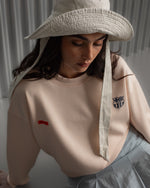 Light pink FC Barcelona sweatshirt with navy club crest on the chest and a small red rectangular detail on the left side.