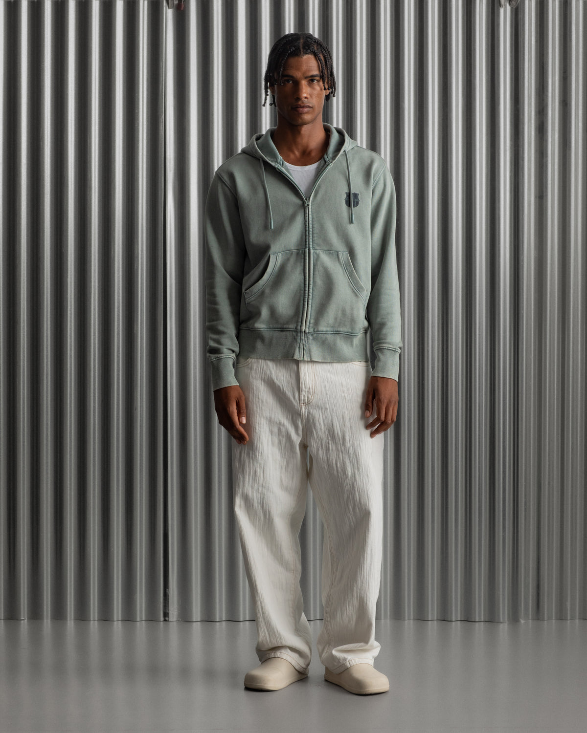 light green FC Barcelona zip-up hoodie with the club’s crest in dark print on the chest, standing against a metallic background.