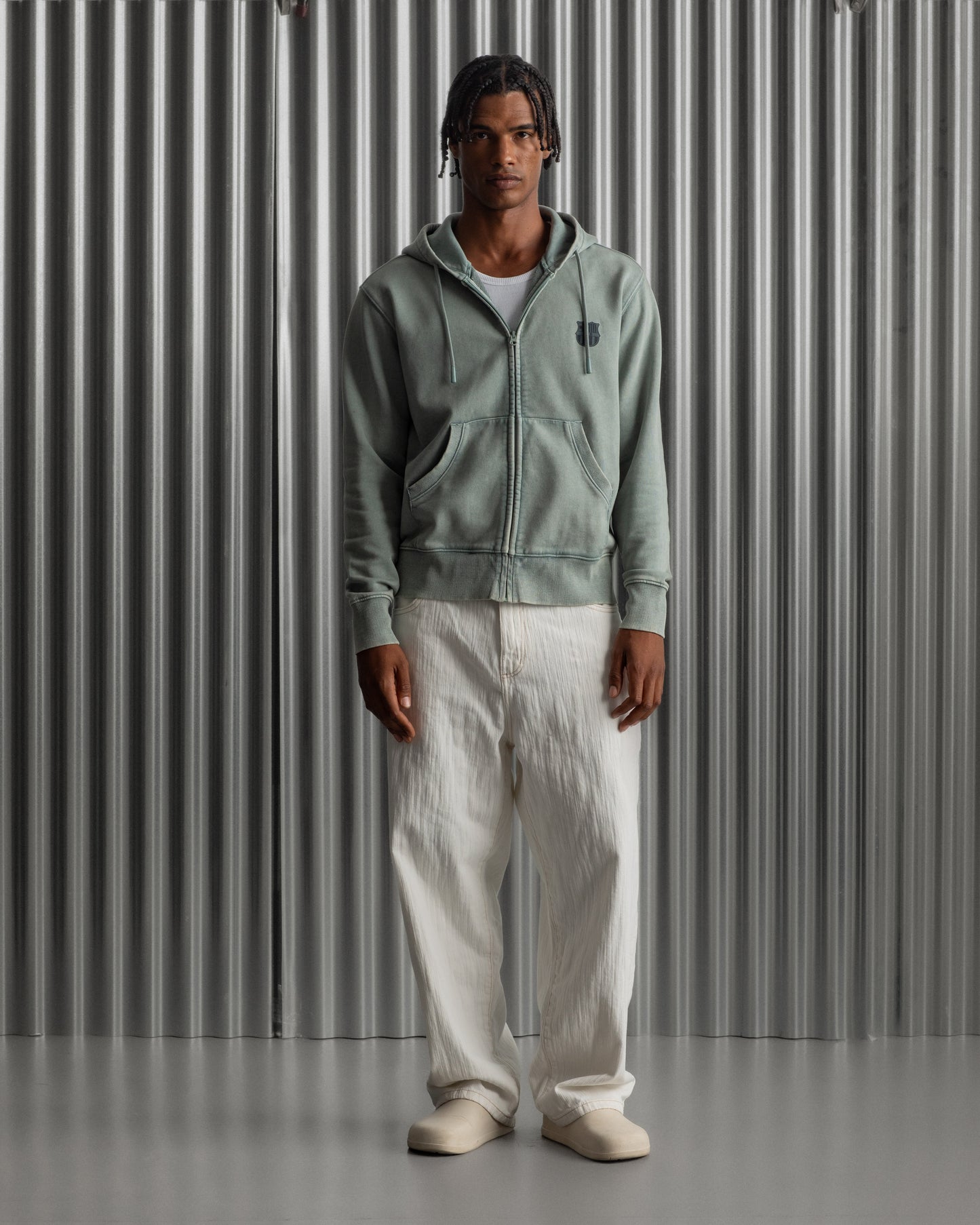 light green FC Barcelona zip-up hoodie with the club’s crest in dark print on the chest, standing against a metallic background.