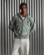 light green FC Barcelona zip-up hoodie with the club’s crest in dark print on the chest, standing against a metallic background.