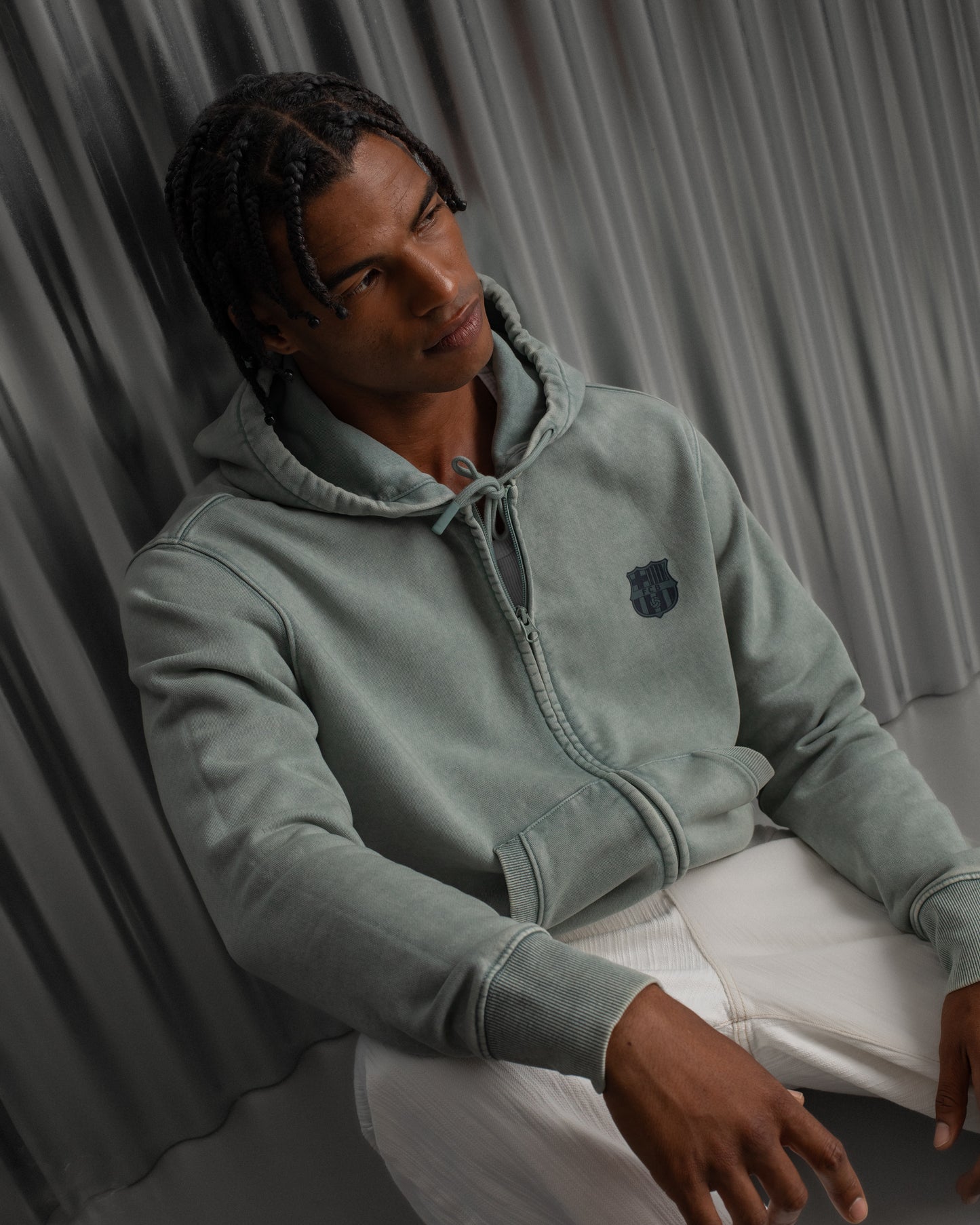 light green FC Barcelona zip-up hoodie with the club’s crest in dark print on the chest, standing against a metallic background.