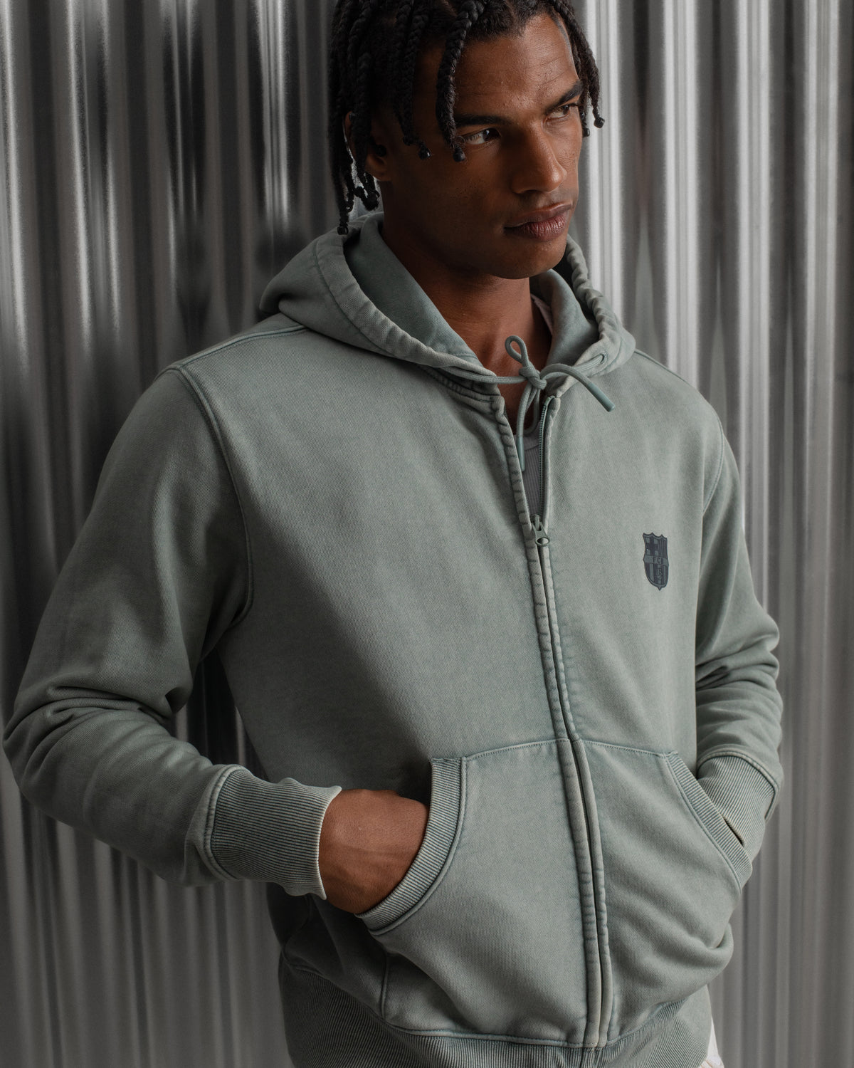 light green FC Barcelona zip-up hoodie with the club’s crest in dark print on the chest, standing against a metallic background.