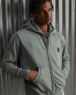 light green FC Barcelona zip-up hoodie with the club’s crest in dark print on the chest, standing against a metallic background.