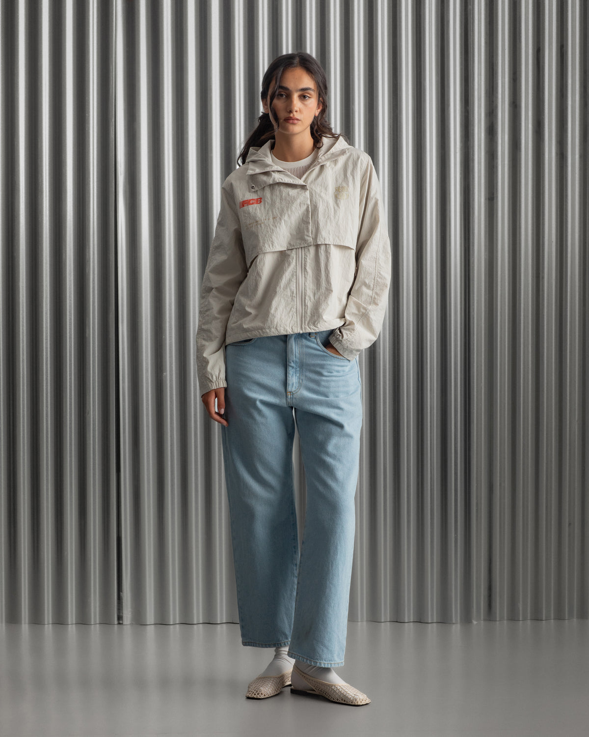 Chaqueta corta beige con capucha del FC Barcelona, cresta bordada en el pecho y detalles gráficos en rojo y dorado, combinada con pantalón vaquero azul claro