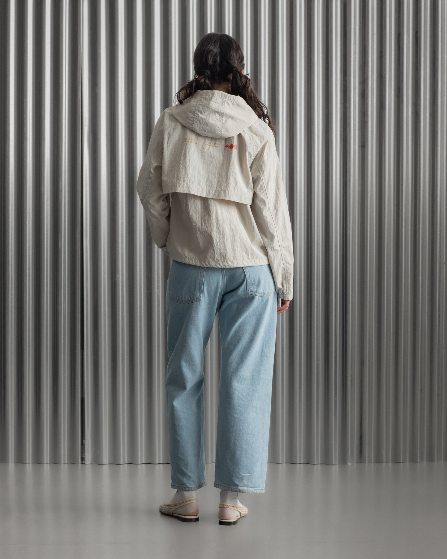 Chaqueta corta beige con capucha del FC Barcelona, cresta bordada en el pecho y detalles gráficos en rojo y dorado, combinada con pantalón vaquero azul claro