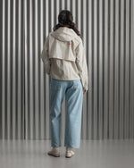 Chaqueta corta beige con capucha del FC Barcelona, cresta bordada en el pecho y detalles gráficos en rojo y dorado, combinada con pantalón vaquero azul claro