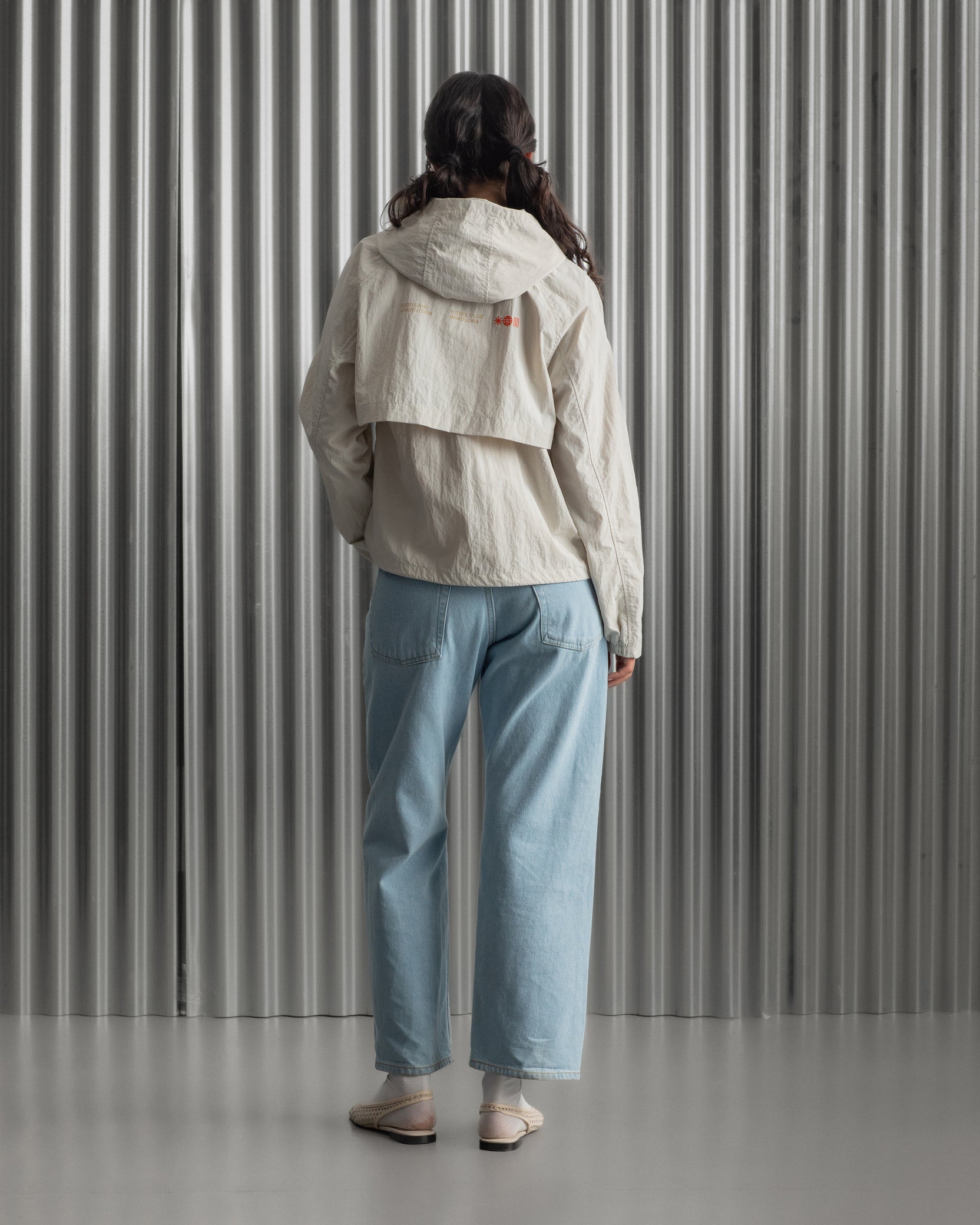 Chaqueta corta beige con capucha del FC Barcelona, cresta bordada en el pecho y detalles gráficos en rojo y dorado, combinada con pantalón vaquero azul claro