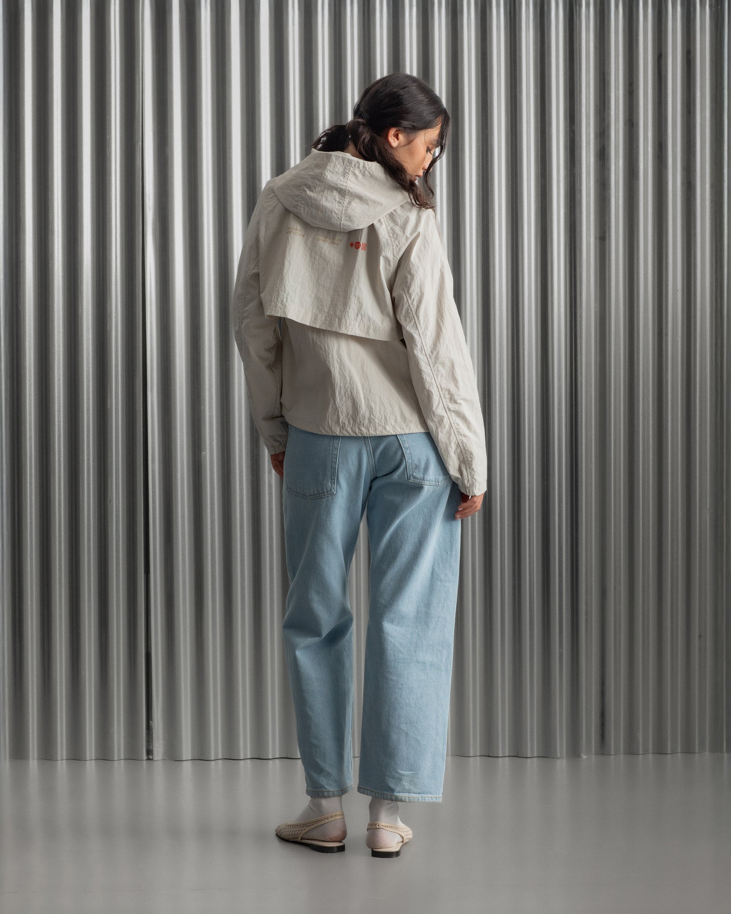 Chaqueta corta beige con capucha del FC Barcelona, cresta bordada en el pecho y detalles gráficos en rojo y dorado, combinada con pantalón vaquero azul claro