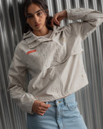 Chaqueta corta beige con capucha del FC Barcelona, cresta bordada en el pecho y detalles gráficos en rojo y dorado, combinada con pantalón vaquero azul claro