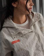 Chaqueta corta beige con capucha del FC Barcelona, cresta bordada en el pecho y detalles gráficos en rojo y dorado, combinada con pantalón vaquero azul claro